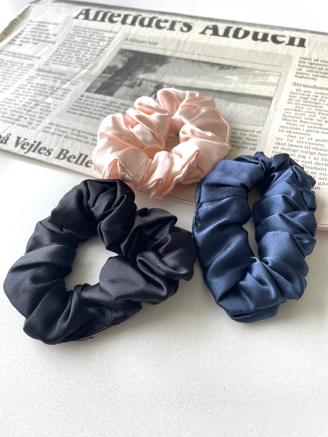 Kvinde iført LA SUIT produkter, herunder marineblå silke scrunchie, marineblå silketørklæde og sort habitjakke set fra siden.