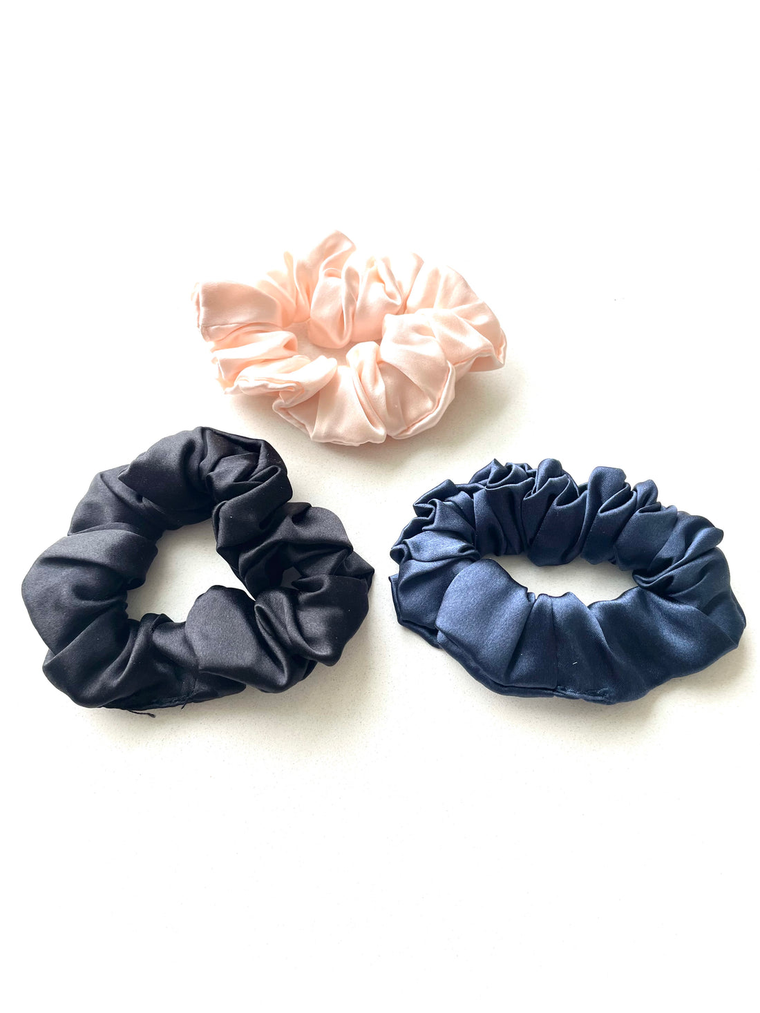 Kvinde iført LA SUIT produkter, herunder marineblå silke scrunchie, marineblå silketørklæde og sort habitjakke set fra siden.